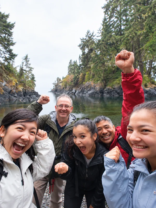 Small travel group cheering beside a forested inlet